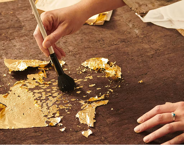 Artisan appliquant des feuilles d’or au pinceau sur une surface texturée